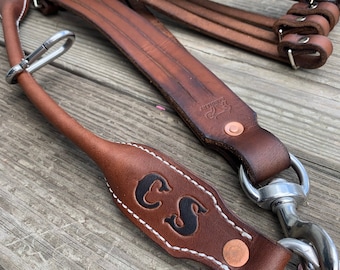 May include: A brown leather camera strap with a metal clasp and a personalized leather patch with the initials "CS".