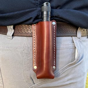 May include: A white ceramic mug with a black handle and the text "But First, Coffee" in a bold, black font. The mug is set against a neutral background, highlighting its simple design.