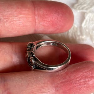 Pu&ograve; includere: Un anello d'argento con un design decorativo. L'anello ha una fascia liscia e lucida e una parte superiore dettagliata con un motivo strutturato. L'anello &egrave; tenuto tra le dita.