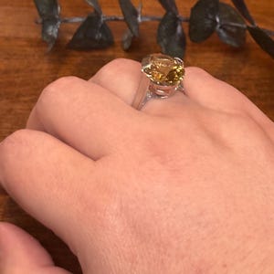Pu&ograve; includere: Un anello in argento con una grande pietra preziosa giallo oro, di forma ovale e sfaccettata, fissata con griffe. La pietra presenta una calda tonalit&agrave; ambrata traslucida con riflessi interni, montata su una fascia in argento lucido.