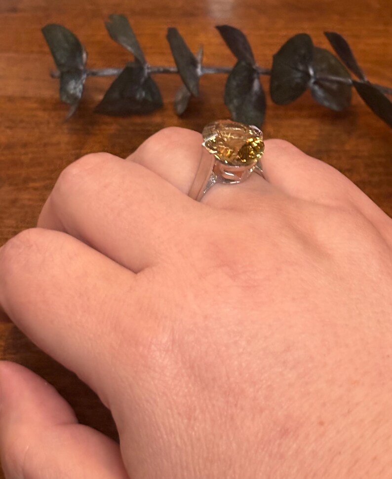 Pu&ograve; includere: Un anello in argento con una grande pietra preziosa giallo oro, di forma ovale e sfaccettata, fissata con griffe. La pietra presenta una calda tonalit&agrave; ambrata traslucida con riflessi interni, montata su una fascia in argento lucido.