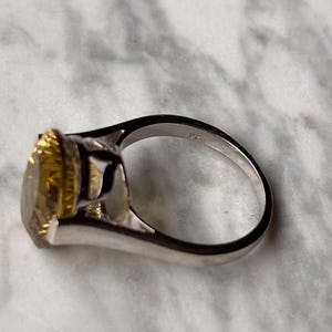 Pu&ograve; includere: Un anello color argento con una grande pietra preziosa gialla a taglio ovale montata su una griffa. L'interno della fascia dell'anello &egrave; chiaramente impresso con il marchio 925, che indica una composizione in argento sterling. Il design presenta una finitura metallica lucida.
