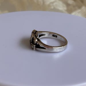 Pu&ograve; includere: Un anello d'argento con un motivo floreale. L'anello presenta un motivo floreale dettagliato sul davanti e il numero "925" &egrave; stampato all'interno della fascia. L'anello &egrave; su una superficie bianca.