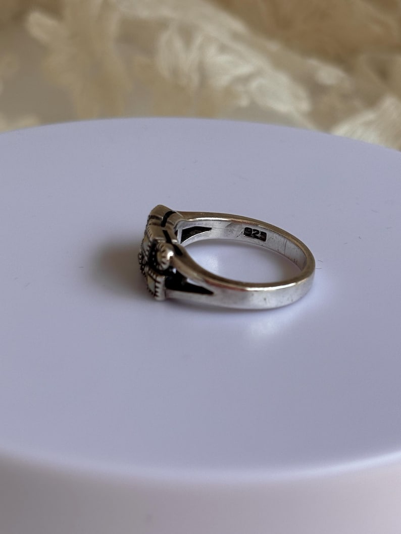 Pu&ograve; includere: Un anello d'argento con un motivo floreale. L'anello presenta un motivo floreale dettagliato sul davanti e il numero "925" &egrave; stampato all'interno della fascia. L'anello &egrave; su una superficie bianca.