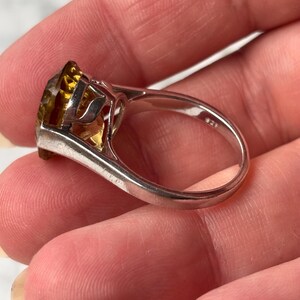 Pu&ograve; includere: Un anello in argento con una grande pietra preziosa giallo oro sfaccettata montata in una incastonatura a griffe. L'interno della fascia dell'anello &egrave; chiaramente marchiato con il punzone 925, che indica una composizione in argento sterling.