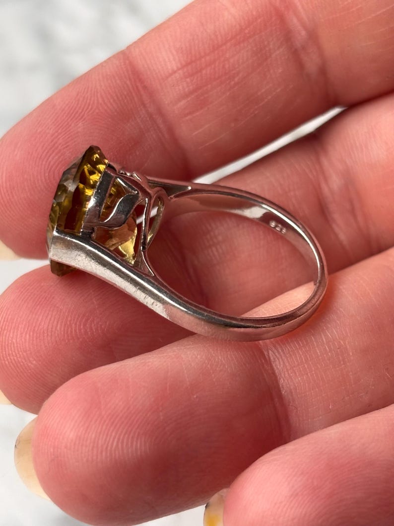 Pu&ograve; includere: Un anello in argento con una grande pietra preziosa giallo oro sfaccettata montata in una incastonatura a griffe. L'interno della fascia dell'anello &egrave; chiaramente marchiato con il punzone 925, che indica una composizione in argento sterling.