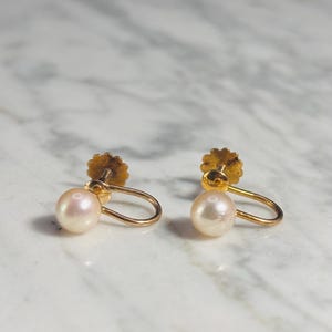 May include: A pair of gold screw-back earrings featuring round, lustrous white pearls. Each earring consists of a polished gold metal loop attached to a threaded post with a decorative, scalloped-edge gold screw mechanism for secure fastening.
