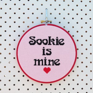 May include: Pink embroidery hoop with red stitching, featuring the text "Sookie is mine" in black lettering and a small red heart.