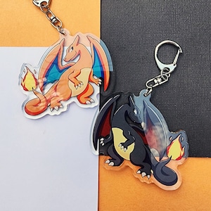 May include: Two clear acrylic keychains featuring cartoon illustrations of the Pokemon characters Charizard and  Blastoise. Charizard is orange with red and blue flames, and Blastoise is blue with a water cannon.