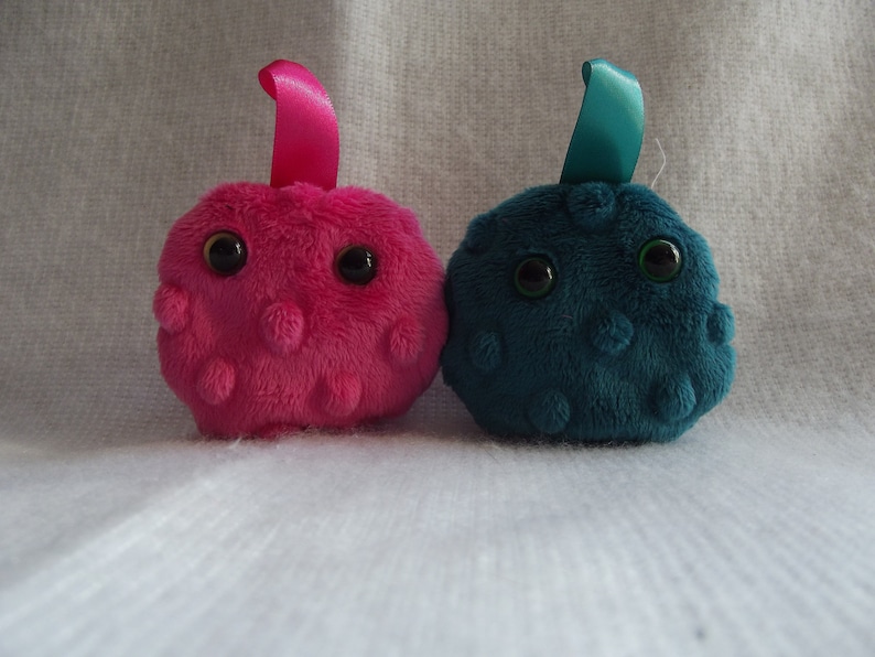 May include: Two plush toys shaped like cells, one pink and one teal blue, with black eyes and a ribbon on top.