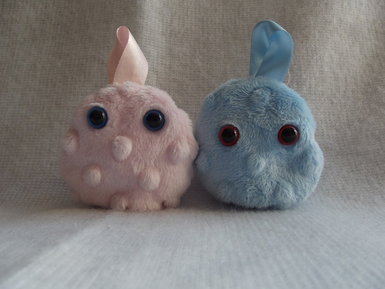 May include: Two plush toys, one pink and one blue, with large black eyes and a fuzzy texture. The pink toy has a pink ribbon on top.