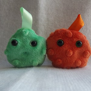 May include: Two plush toys shaped like cells. One is green with a green ribbon and the other is orange with an orange ribbon.