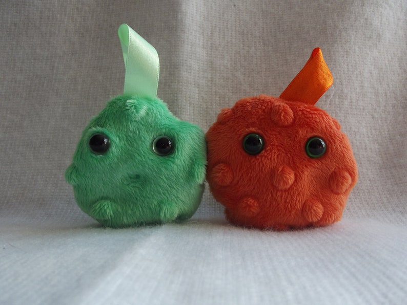 May include: Two plush toys shaped like cells. One is green with a green ribbon and the other is orange with an orange ribbon.