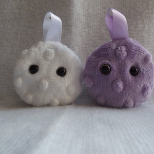 May include: Two plush toys shaped like round balls with googly eyes. One is white with white dots and the other is purple with purple dots.