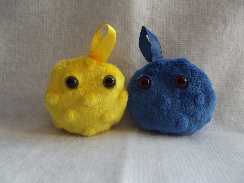 May include: Two plush toys shaped like cells. One is yellow with black eyes and the other is blue with red eyes.
