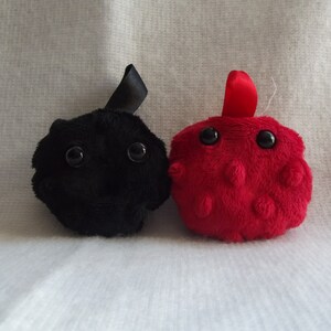 May include: Two plush toys, one black and one red, with large eyes and a round shape. The black toy has a black ribbon on top, and the red toy has a red ribbon on top.