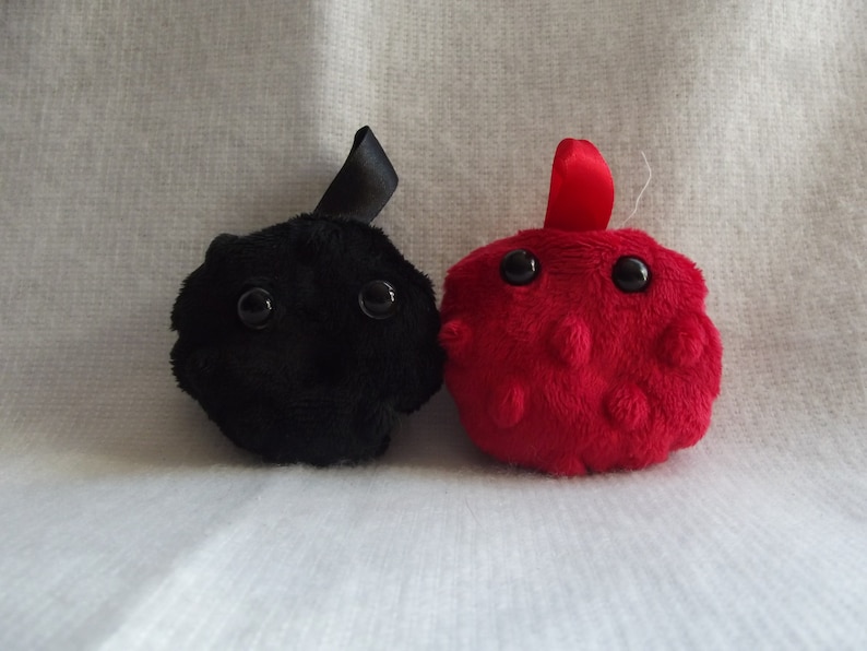 May include: Two plush toys, one black and one red, with large eyes and a round shape. The black toy has a black ribbon on top, and the red toy has a red ribbon on top.