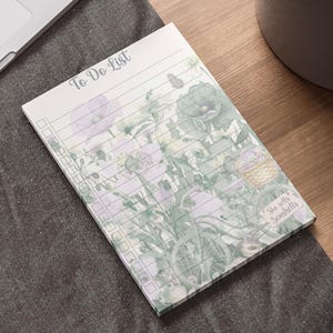 May include: A floral-themed To Do List notepad with a bicycle and basket design. The notepad features a soft color palette of green, purple, and white. The text "To Do List" is at the top, and "She sells Seashells" is at the bottom.