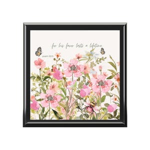 Puede incluir: Una impresión floral enmarcada con flores rosas, mariposas y el texto "for his favor lasts a lifetime" y "psalm 30:5". La obra de arte tiene un marco negro y un fondo blanco.