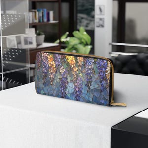 May include: A rectangular wallet with a stained glass design featuring purple, yellow, and blue wisteria flowers. The wallet has a gold zipper and a black border. The design is reminiscent of a mosaic.