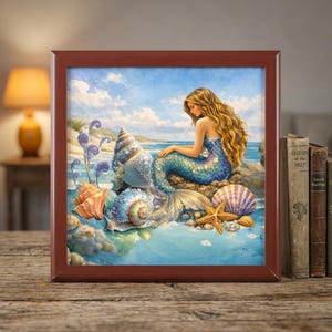 Könnte beinhalten: Ein gerahmter Druck mit einer Meerjungfrau mit langen, fließenden blonden Haaren und einem blau-türkisfarbenen Schwanz, die zwischen Muscheln und Seesternen sitzt. Das Kunstwerk hat ein Küstenmotiv mit blauem Himmel und Ozeanhintergrund.