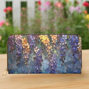 May include: A zippered wallet featuring a mosaic-style floral design with purple, yellow, and blue wisteria blooms. The wallet has a gold-colored zipper and a rectangular shape. The background is blurred, with a wooden surface.
