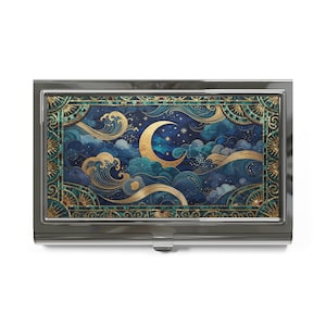 May include: A rectangular metal business card case featuring a dark blue and teal night sky illustration with a golden crescent moon, swirling clouds, and stylized waves. The design is framed by a decorative border with gold and teal geometric patterns.