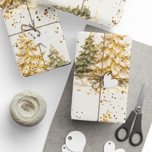 Peut inclure: Deux cadeaux rectangulaires emballés dans du papier blanc avec une forêt peinte de sapins verts et de paillettes dorées. Les paquets sont liés avec de la ficelle brune, l'un avec une étiquette étoile blanche et l'autre avec un cœur, avec des ciseaux.