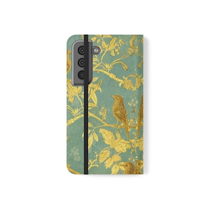 May include: A rectangular phone case featuring a teal background with a repeating gold pattern of birds perched on branches with leaves. A black vertical elastic strap runs along the left side, and the camera cutout is visible at the top left.