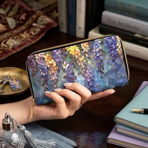May include: A rectangular zip-around wallet with a mosaic-style floral design in shades of purple, blue, yellow, and green. The wallet has a gold-colored zipper and a matching pull tab.