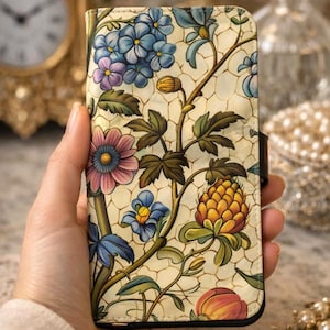 May include: A rectangular phone case featuring a cream-colored background with a crackled texture pattern. The surface is decorated with colorful illustrations of blue, purple, and pink flowers, green leaves, and a textured yellow fruit.