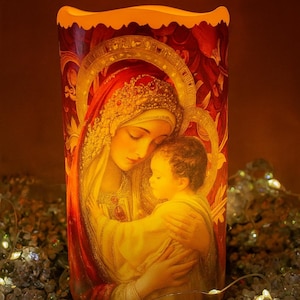 May include: A religious candle with a warm glow, featuring an image of Mary and baby Jesus. The artwork is in shades of red, gold, and yellow, with a halo around the figures. The candle is surrounded by decorative lights.