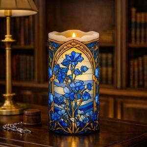 May include: A cylindrical candle with a stained-glass design featuring blue floral patterns. The candle has a cream-colored top with a flickering LED light. The design is framed by gold and blue accents, creating a decorative and elegant look.