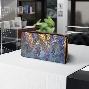 May include: A zippered wallet featuring a stained-glass style floral design in shades of purple, yellow, and blue. The wallet has a gold-colored zipper and a black border. The design depicts hanging wisteria flowers.
