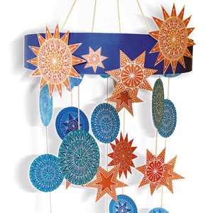 Op de afbeelding: Een blauwe en oranje papieren mobiel met sterren en cirkels die aan een blauwe ring hangen. De sterren en cirkels hebben ingewikkelde patronen.