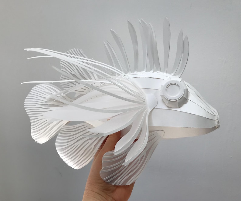 May include: A white paper sculpture of a fish with intricate details and a spiky fin. The fish is made of folded paper and has a realistic appearance.