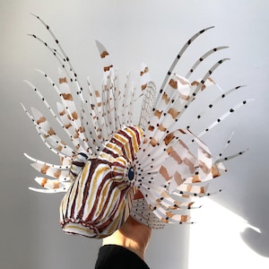May include: A papercraft model of a lionfish with white, brown, and black stripes and spots. The model is made of paper and has a realistic appearance.