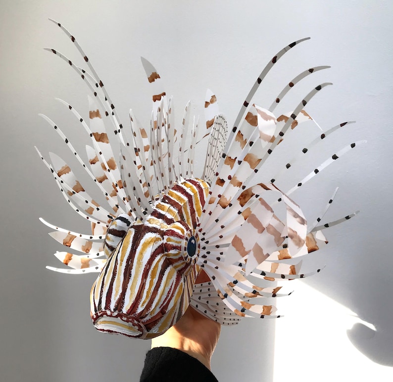 May include: A papercraft model of a lionfish with white, brown, and black stripes and spots. The model is made of paper and has a realistic appearance.