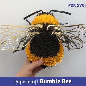 Puede incluir: Una abeja de papel con un cuerpo difuso amarillo y negro y alas translúcidas con bordes dorados. El texto PDF, SVG files es visible en la esquina superior derecha, y el texto Paper craft Bumble Bee está en la parte inferior.