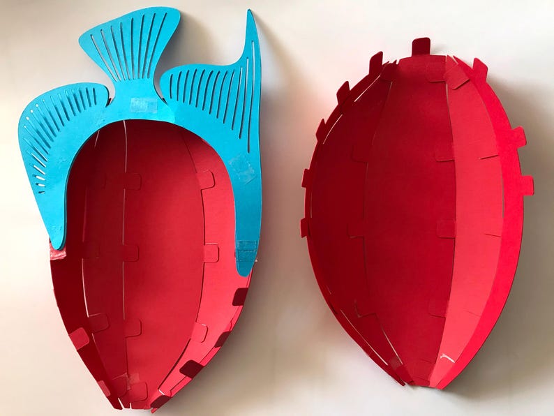 May include: Two red, bowl-shaped containers with a curved, segmented design. One container features a bright blue, decorative fish-shaped attachment on its upper edge, while the other is a plain red, oval-shaped bowl with small tabs along the rim.