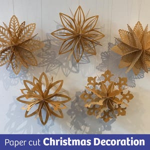 May include: Five hanging, gold-coloured paper cut Christmas decorations. The decorations are in the shape of stylized flowers and snowflakes. The text "Paper cut Christmas Decoration" is at the bottom of the image.
