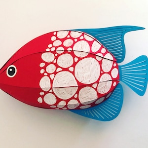 May include: A three-dimensional fish sculpture featuring a vibrant red body decorated with white circular patterns. The fish has a black and white eye and bright blue fins with linear cutouts, creating a layered and structured appearance.