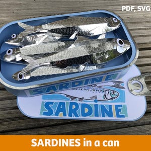 Könnte beinhalten: Eine hellblaue Sardinenbüchse mit dem Wort "SARDINE" auf dem Deckel. Im Inneren der Dose befinden sich mehrere silberne Fische. Die Dose ist geöffnet und zeigt die Sardinen. Der Text "PDF, SVG files" ist ebenfalls enthalten.