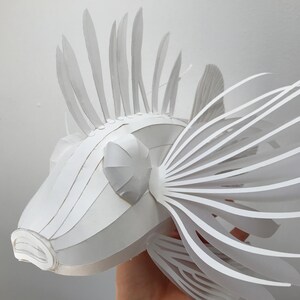 May include: A white paper sculpture of a lionfish with intricate details. The sculpture is made of folded paper and has a realistic appearance.