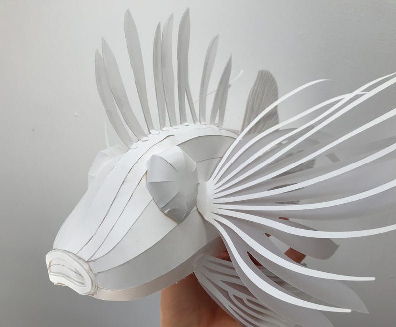May include: A white paper sculpture of a lionfish with intricate details. The sculpture is made of folded paper and has a realistic appearance.