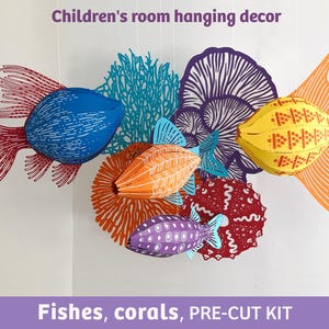May include: A hanging mobile featuring three-dimensional paper fish and coral shapes in blue, orange, yellow, purple, and red. The set includes a blue fish with red fins, an orange fish, a purple fish, and various coral structures. Text reads: Children's room hanging decor. Fishes, corals, PRE-CUT KIT.