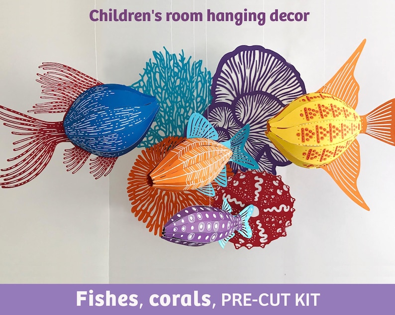 May include: A hanging mobile featuring three-dimensional paper fish and coral shapes in blue, orange, yellow, purple, and red. The set includes a blue fish with red fins, an orange fish, a purple fish, and various coral structures. Text reads: Children's room hanging decor. Fishes, corals, PRE-CUT KIT.