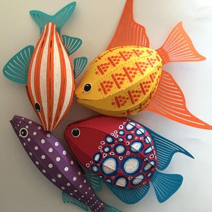 May include: Four decorative paper fish sculptures. One is orange and white striped with teal fins, one is yellow with red dotted patterns and orange fins, one is purple with white polka dots, and one is red with blue and white circular patterns.