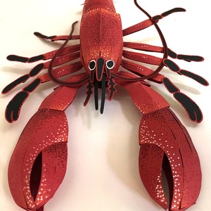 Peut inclure: Un homard en papier rouge avec des yeux et des pattes noirs. Le homard est fait de papier et a une surface textur&eacute;e.