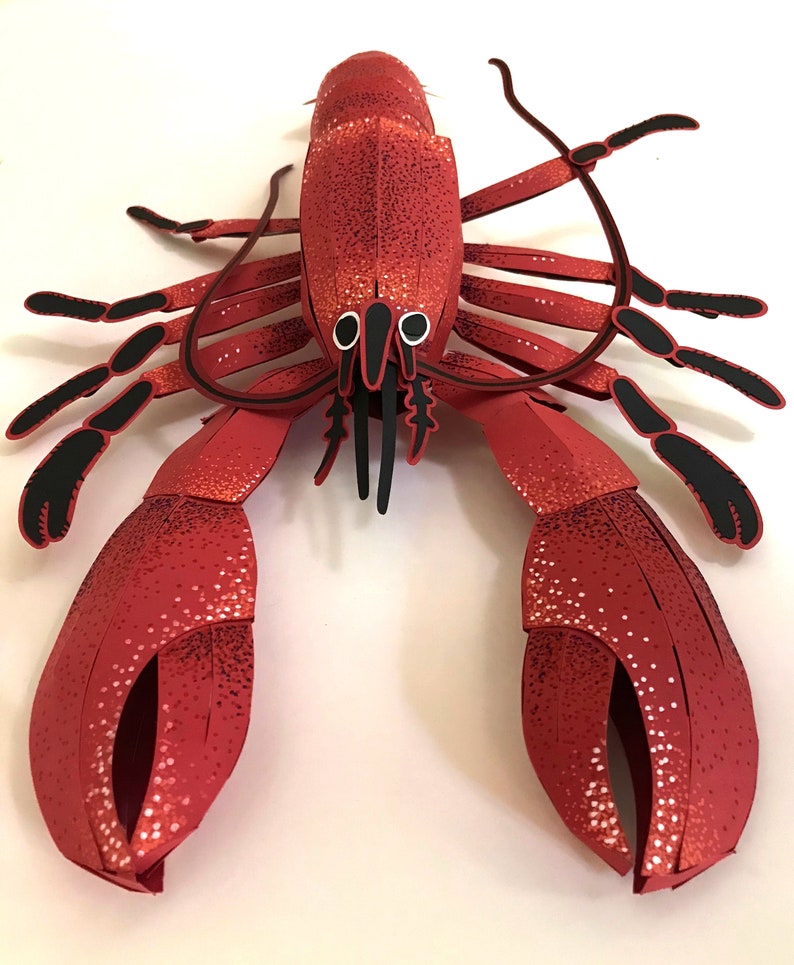 Peut inclure: Un homard en papier rouge avec des yeux et des pattes noirs. Le homard est fait de papier et a une surface textur&eacute;e.